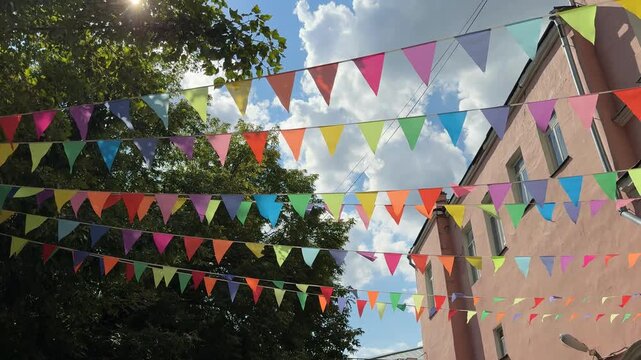 Colorful triangular flags hanging outdoors with blue sky and clouds in summer background