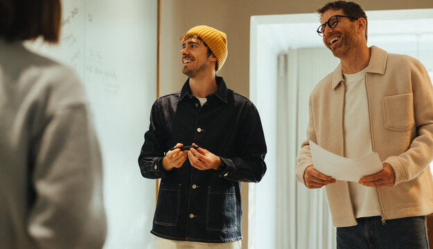 Coworkers discuss ideas at a whiteboard during an office brainstorming meeting
