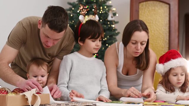 Happy family cut paper snowflakes near Christmas tree, celebrating Christmas with together. New Year's preparations and decorations. Paper crafts.