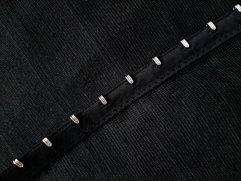 Close-up macro photograph of metal hook-and-eye closures on black corset fabric.