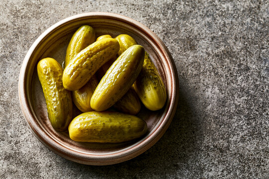 Artisan pickled cucumbers arranged on a ceramic plate with textured surface