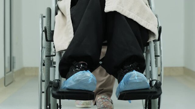 Nurse takes woman in wheelchair to sterile procedure room. Woman moves wheelchair toward modern procedure room in medical center. Slow motion
