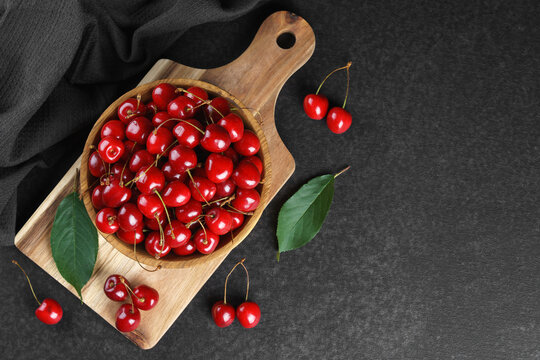 Fresh ripe sweet cherries in rustic wooden bowl with green leaves on black textured background. Top view flat lay with copy space. Juicy organic summer fruit, red berries, healthy seasonal food