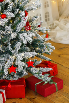 Frosted Christmas tree decorated with red stars, red baubles and warm fairy lights, with wrapped presents with gift boxes on wooden floor in cozy room. Holiday mood, festive aesthetic atmosphere