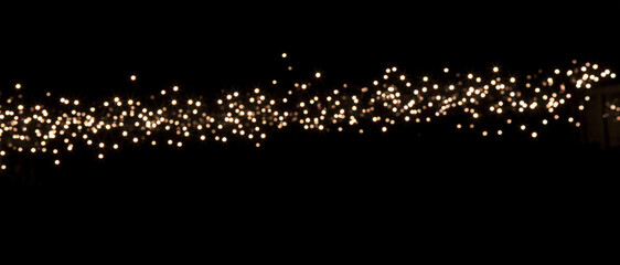 Naklejka premium Horizontal border of glowing fairy lights against black background. Sparkling bokeh garland with warm white festive illumination. Abstract holiday banner with copy space