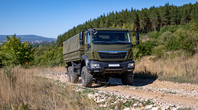 Large military cargo truck with a tarpaulin covered rear compartment driving toward the camera on a rugged dirt road, dramatic open landscape combining dry grass, forest and distant hills, dust trai