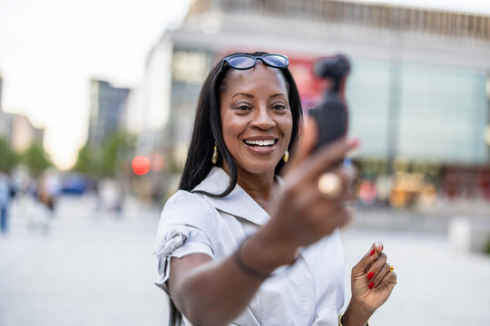 Woman filming a vlog in the city using a pocket-sized camera
