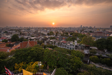 Obraz premium Panoramic view over Bangkok from Wat Saket Golden Mount in Thailand, overlooking traditional rooftops, historic neighborhoods and the sprawling urban cityscape during warm evening light.
