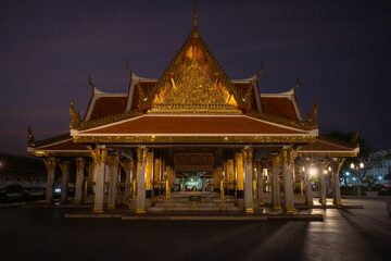 Obraz premium Traditional Thai Buddhist temple illuminated at night in Bangkok, Thailand, showcasing ornate architecture, golden details and spiritual atmosphere.
