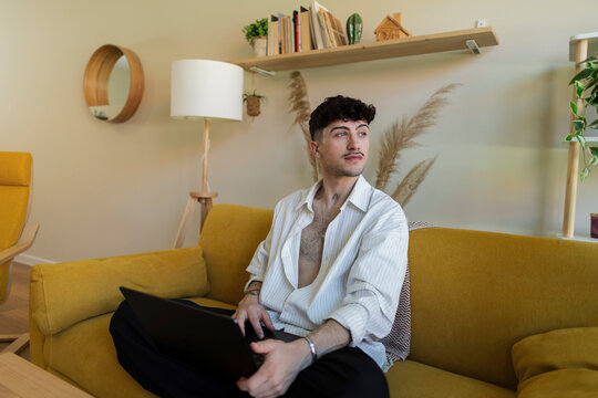 Young man contemplating while working on laptop at home