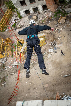 Man in helmet rope jumping with arms spread over abandoned construction debris field, extreme sport adrenaline and thrill concept