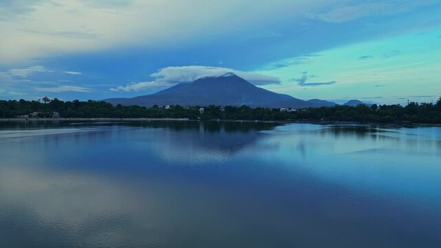 Low-altitude drone panoramic entrance of the Sampaloc Lake. Capture a perfect mirror reflection of the sky framing Mount San Cristobal majestically in the background during clear sky to blue hour.
