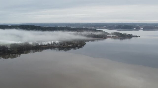 Aerial drone shot showing Lake Anten near Grafsnas with mist floating above the shoreline and calm water surrounded by winter countryside in Alingsas, Sweden
