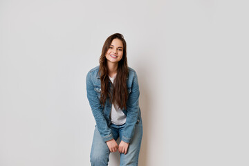 Obraz premium Brunette girl dressed in blue denim and white t-shirt smiles confidently in studio