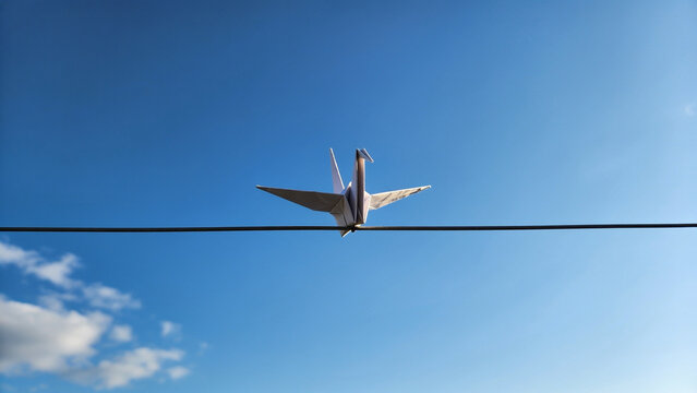 White paper crane standing on a thin wire against a bright blue clear sunny sky background