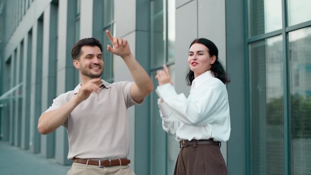Two happy Caucasian business colleagues male with female dancing active smiling in city. Cheerful man with woman dance together businessman with businesswoman partners smile optimistic moving outside