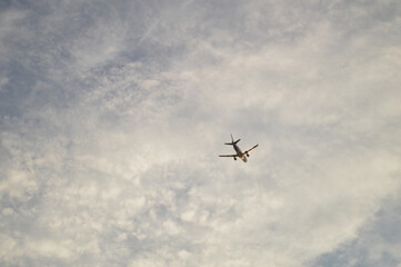 Fototapeta premium Commercial passenger jet airplane flying overhead through a partly cloudy overcast sky, viewed from the ground looking upward in natural daylight
