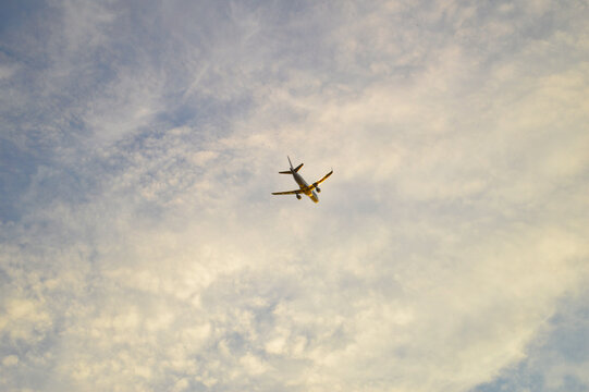 Commercial passenger airplane flying overhead against a partly cloudy blue sky, captured from below in warm golden afternoon light