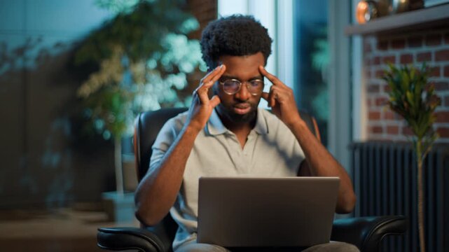 Bad feeling African American business man using laptop feeling headache at evening home office unhealthy stressed businessman male guy work online with computer suffering migraine head painful disease