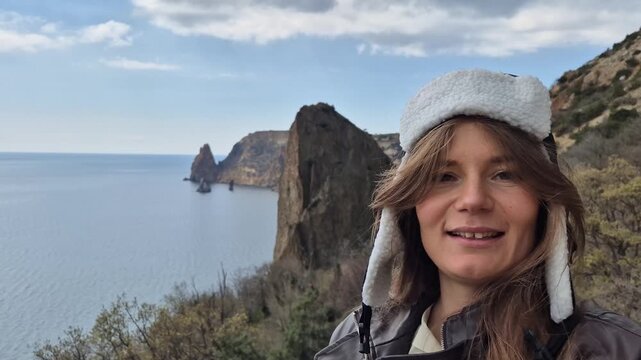 Woman traveler waving hello at scenic Fiolent coastal cliff overlooking Black Sea. Selfie angle handheld shot.