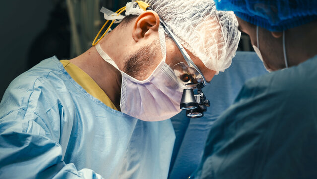Focused surgeon uses professional surgical loupes for enhanced magnification and precision during a medical operation in a hospital.