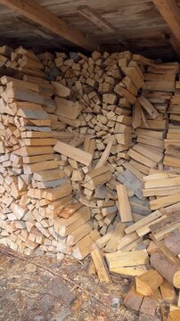 Gestapeltes Brennholz zur trockenen Lagerung f&uuml;r die Heizsaison - Gro&szlig;e Mengen gespaltenes Brennholz lagern trocken unter einem Unterstand. Holzvorrat zum Heizen mit Kamin oder Holzofen w&auml;hrend der ka