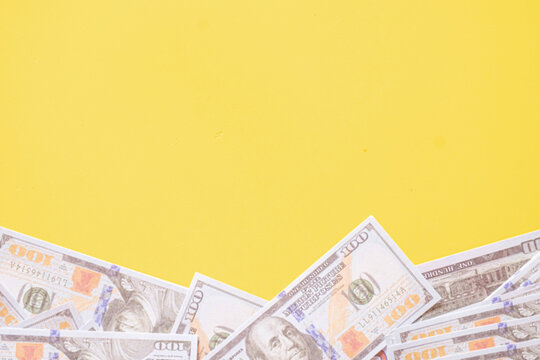 Top view of hundred US dollar bills border at the bottom on a yellow background with copy space. Concept of finance, wealth, business investment, budget, and making money.