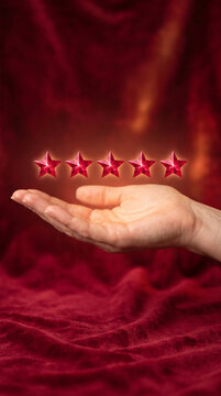 Open hand holding five glowing red stars, symbolizing top rating or excellent quality, against a rich red fabric background