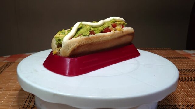Traditional Chilean completo italiano hot dog rotating on a turntable, sausage with avocado, tomato and mayonnaise, popular Chilean street food