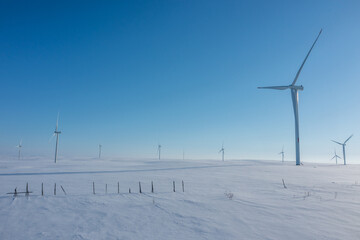 Fototapeta premium Close drone perspective of modern wind turbines standing tall across a vast, pristine snow-covered field under a clear blue sky.