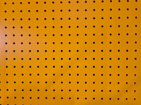 Bright orange pegboard with evenly spaced holes. Uniform pattern creates clean, industrial aesthetic. Ideal for storage, workshop, or creative project backgrounds