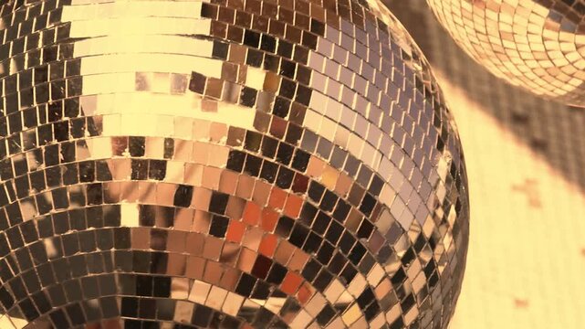 Two disco balls hang from a ceiling reflecting warm golden evening light