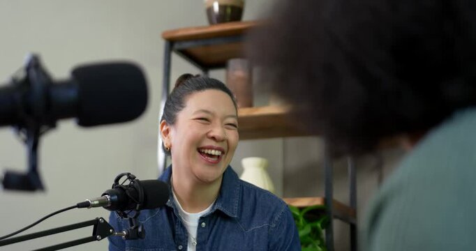 Adult Asian woman reacting to host, laughing, listening, answering into mic in studio in denim