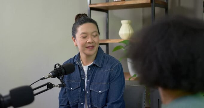 Asian woman listening then answering after African American interviewer speaking into mic in studio
