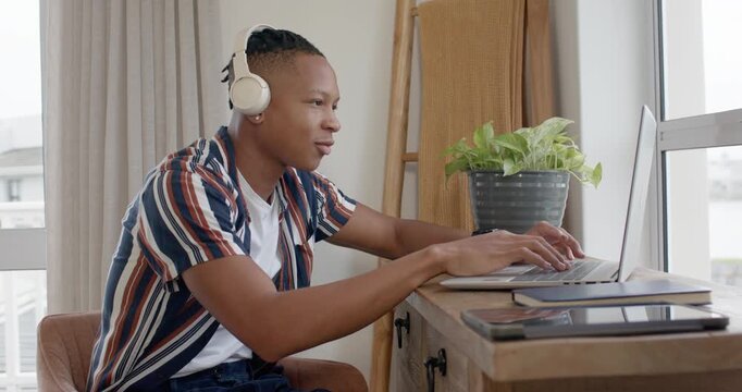African American man after typing at laptop by window tilting screen, removing headset and resting