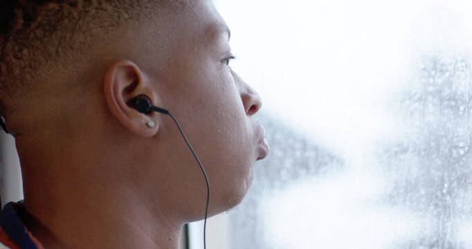 African American man sitting beside wet window striped polo wired buds puffing relaxing, copy space