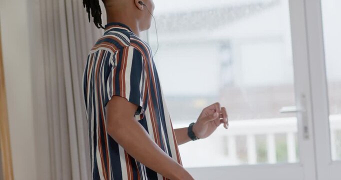 African American man in striped shirt plugging wired earbud by sliding door, phone playing music