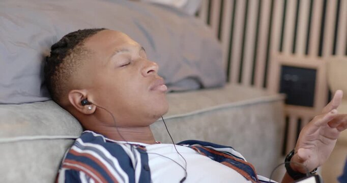 African American man reclining on daybed, listening with wired earphones, moving right hand gently