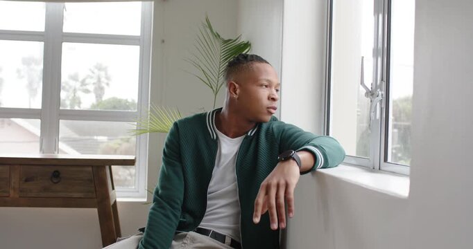 African American man showing stress sitting by window covering face leaning on sill seeking calm