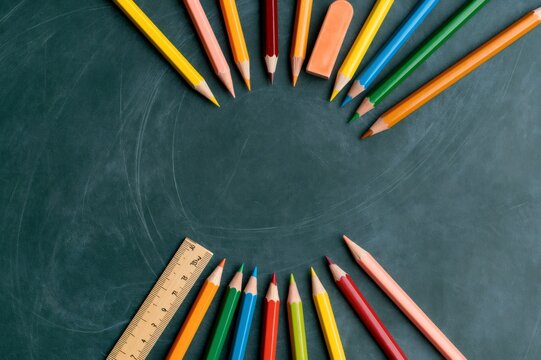 Colorful pencils and school supplies forming circle on chalkboard