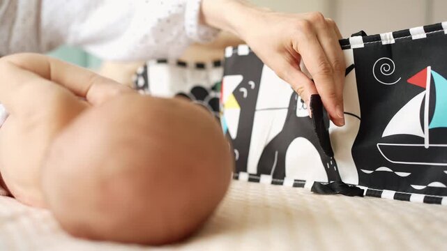 Close up of a mother showing a high contrast black and white book to her newborn baby for visual stimulation, promoting early learning and cognitive development in the infant