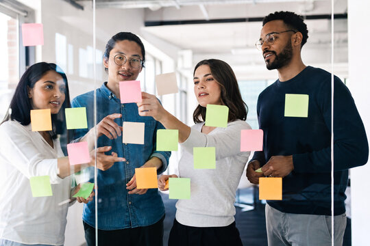 Diverse Business Team Brainstorming Creative Ideas with Colorful Sticky Notes on a Glass Wall in a Bright Contemporary Office Workspace