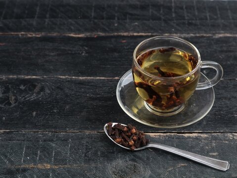 A glass cup of aromatic clove tea served with a spoonful of whole dried cloves on a dark wooden background. Perfect for herbal remedy, wellness, healthy drink, spice, and natural medicine themes