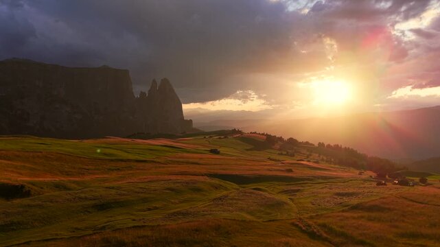 Sunset over Sciliar above Alpe di Siusi in the Dolomites, with golden alpine meadows, dramatic clouds and warm light creating a scenic mountain landscape.