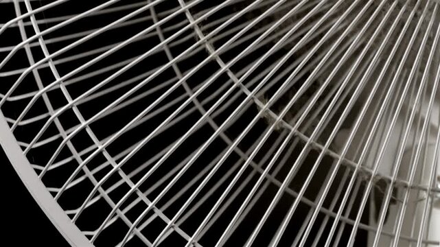 White oscillating fan grille moves across a dark background in close-up.