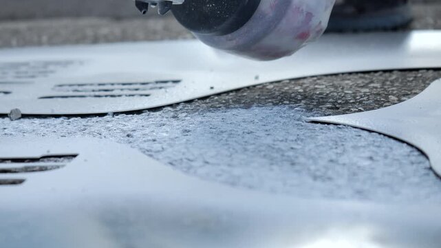 Close-up of a street artist spraying paint through a stencil on pavement, revealing a graphic design in an urban graffiti and street art creation process.