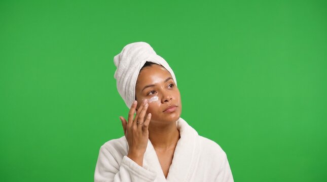 Medium close up frontal portrait photo of a dark-skinned Black young adult woman in Generation Z with a white towel turban and white bathrobe, looking upward with a relaxed expression while dotting co