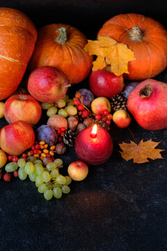 burning candle, ripe fruits, pumpkins, nuts, fallen leaves close up on dark background. Witchcraft, esoteric spiritual ritual for fall season, Mabon Holiday. symbol of Harvest, Thanksgiving