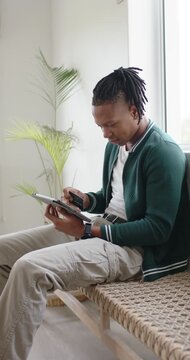 Vertical video: Adult African American man sitting on bench tapping tablet, withdrawing card to pay