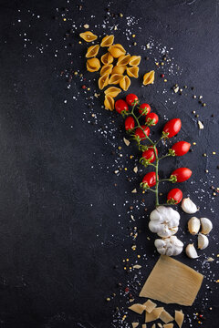 Ingredients for cooking pasta on a black background. Pasta, sherry tomatoes, garlic, cheese, pepper and salt.